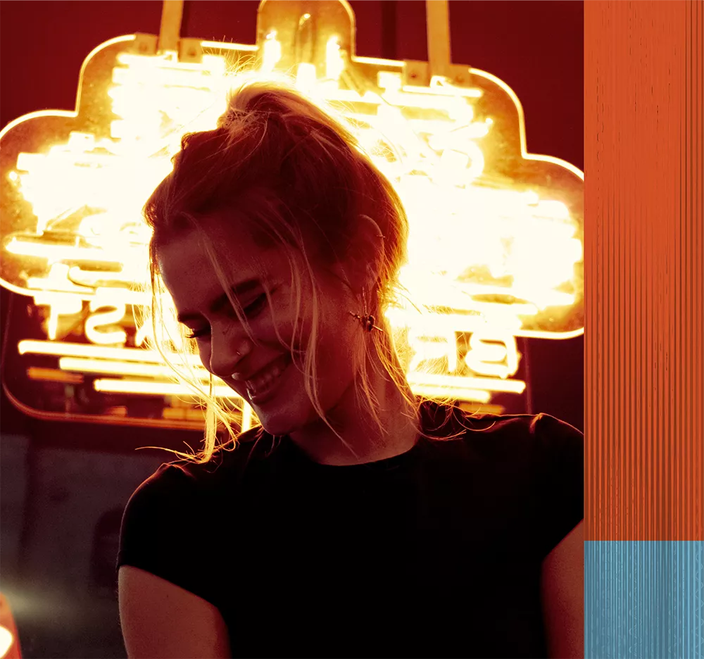 Photo of stylish woman smiling with a neon sign behind her